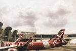 AirAsia aircraft parked at airport terminal gate with red and white livery under overcast sky