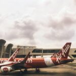 AirAsia aircraft parked at airport terminal gate with red and white livery under overcast sky