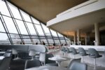 Spacious airport lounge with panoramic windows, bar seating, and passengers relaxing before flights