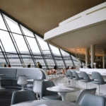 Spacious airport lounge with panoramic windows, bar seating, and passengers relaxing before flights