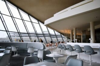 Spacious airport lounge with panoramic windows, bar seating, and passengers relaxing before flights