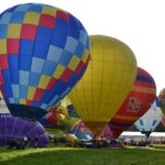 Hot air balloons inflating at a UK balloon festival, with colourful patterns and crowds gathered on a grassy field.