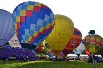Hot air balloons inflating at a UK balloon festival, with colourful patterns and crowds gathered on a grassy field.