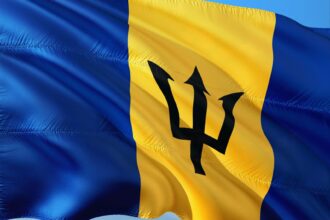 Barbados flag with blue background and yellow stripe containing black trident symbol waving against sky