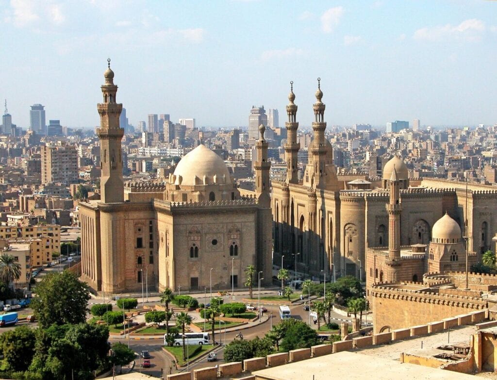 Historic mosque with multiple minarets and domes overlooking modern Cairo cityscape