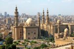 Historic mosque with multiple minarets and domes overlooking modern Cairo cityscape