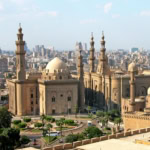 Historic mosque with multiple minarets and domes overlooking modern Cairo cityscape