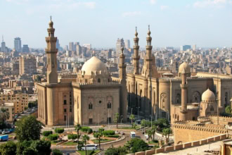 Historic mosque with multiple minarets and domes overlooking modern Cairo cityscape