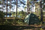 Green camping tent set up in a pine forest beside a lake
