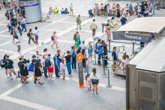 Travellers queue to buy attraction tickets at a popular tourist destination using city passes and mobile ticket apps.