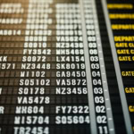 Close-up of an airport departure board showing flight numbers and gate statuses in yellow text