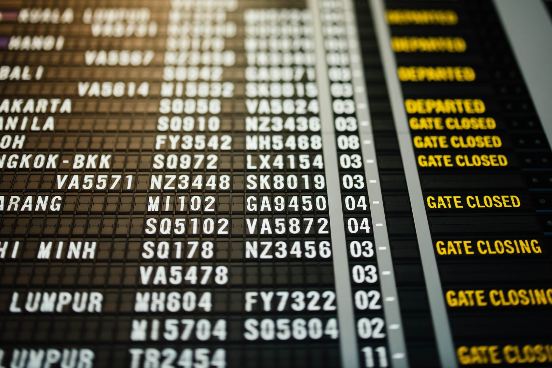 Close-up of an airport departure board showing flight numbers and gate statuses in yellow text