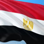 Egyptian flag with red, white, and black horizontal stripes and golden eagle emblem waving in the wind