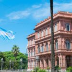 Pink neoclassical Casa Rosada presidential palace in Buenos Aires with Argentine flag flying and palm trees under blue sky