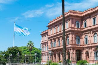 Pink neoclassical Casa Rosada presidential palace in Buenos Aires with Argentine flag flying and palm trees under blue sky