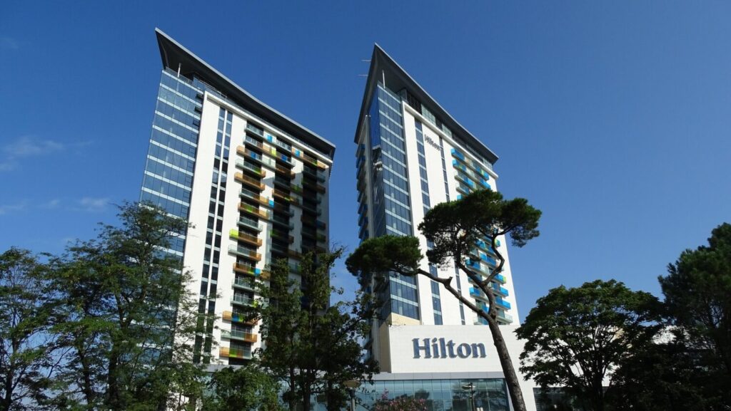 Hilton Batumi twin-tower hotel with glass facade and colourful balconies, set against a clear blue Georgian sky.