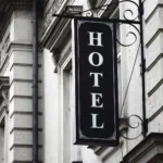 Black and white vertical hotel sign mounted on a historic stone building facade