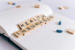 Wooden scrabble tiles spelling ‘Health Insurance’ on a calendar with blue pills, symbolising travel insurance preparation and medical coverage planning