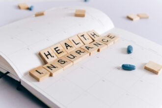 Wooden scrabble tiles spelling ‘Health Insurance’ on a calendar with blue pills, symbolising travel insurance preparation and medical coverage planning