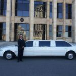 Chauffeur in black suit standing beside white stretch limousine outside Parliament of Western Australia building