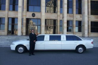 Chauffeur in black suit standing beside white stretch limousine outside Parliament of Western Australia building