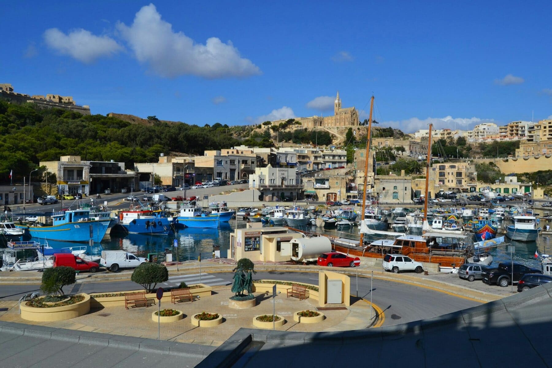 Boats in Mgarr Harbour with church on the hilltop in Gozo, Malta