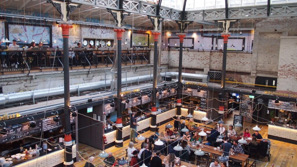 Interior of Mackie Mayor food hall in Manchester’s Northern Quarter, featuring independent vendors, communal tables, and a restored Victorian market hall design.