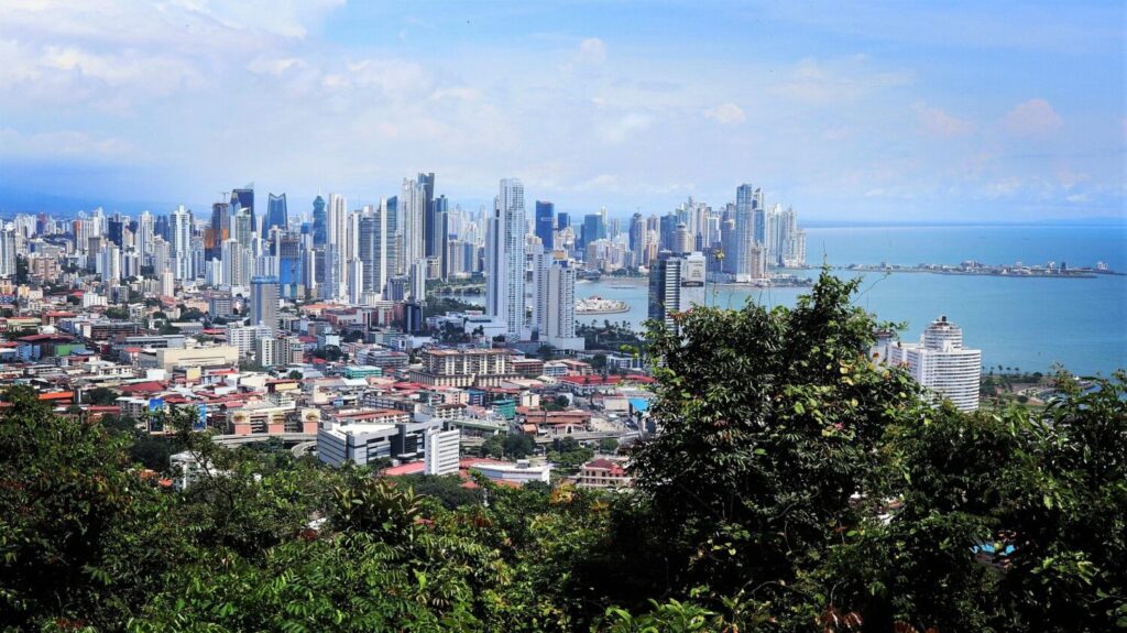 Panoramic view of Panama City skyline with modern skyscrapers along the coastline, viewed from hillside with tropical vegetation
