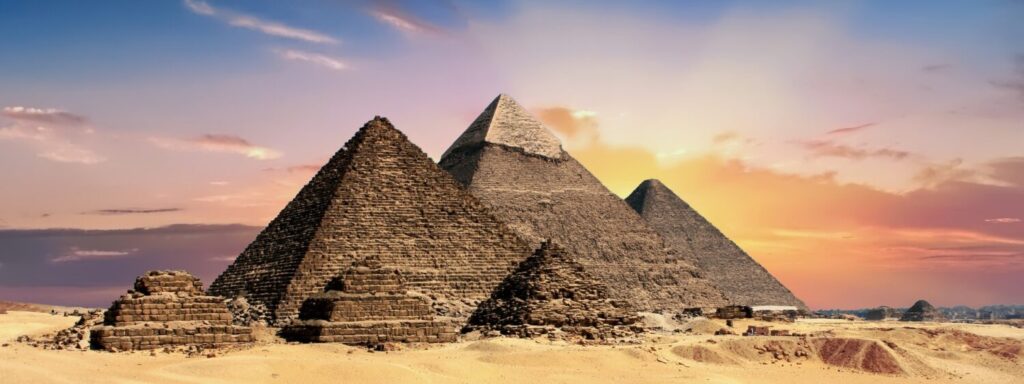 The three Pyramids of Giza in Egypt at sunset, with desert terrain in the foreground.