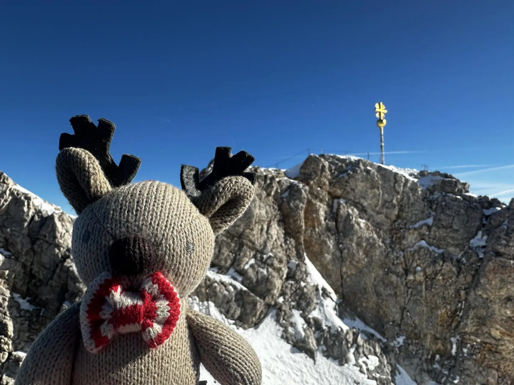 Rupert the reindeer at Zugspitze summit with golden cross in background