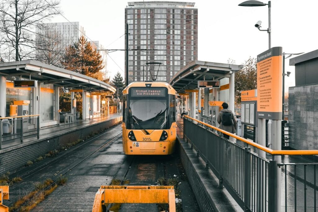 Orange and grey Metrolink tram number 3015 at Salford Quays station platform with modern station architecture and apartment buildings in background