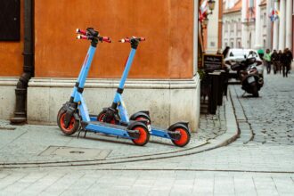 Two parked electric scooters with red wheels on a cobblestone street corner in a European city