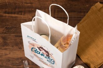 White paper bakery bag with bread and drink inside, on wooden table