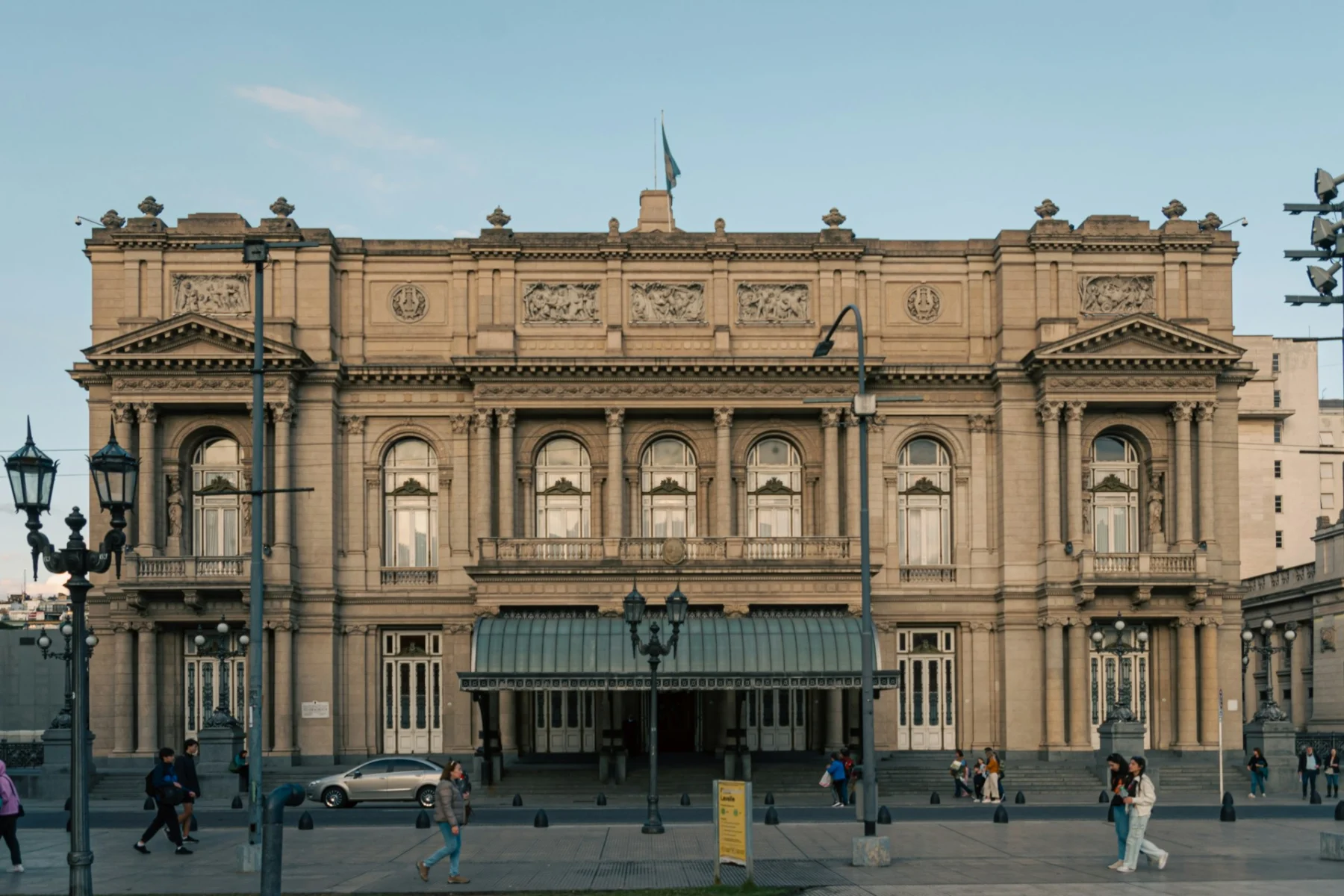 Classical facade of Teatro Colón opera house in Buenos Aires with ornate neoclassical architecture and visitors in the plaza