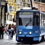 Blue tram passing through a busy street in Zagreb, Croatia, with pedestrians and historic buildings in the background