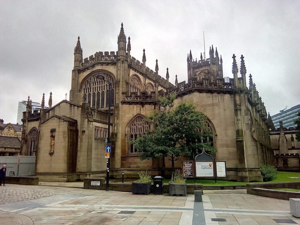 Exterior of Manchester Cathedral in Manchester, showing Perpendicular Gothic stonework and tracery on an overcast day.