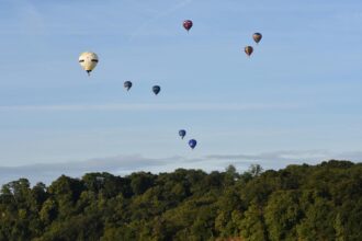 Hot air balloons rising over trees at the Bristol International Balloon Fiesta