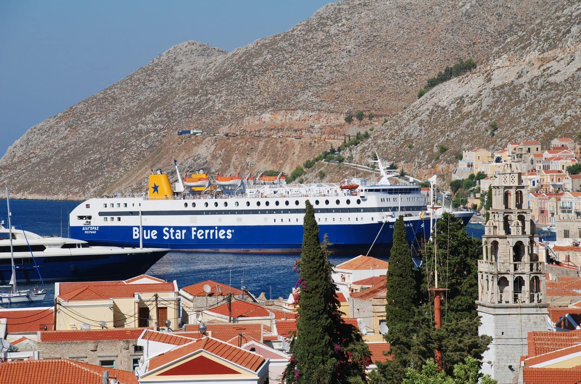 Blue Star Ferries ship arriving at Symi Island harbour with hillside houses in the background