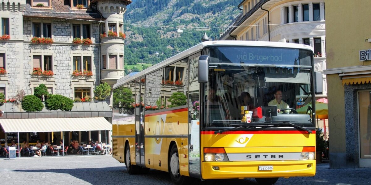 Bright yellow Swiss PostBus in a mountain town square, ideal for illustrating intercity and rural coach travel featured in the Busbud app guide.