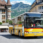 Bright yellow Swiss PostBus in a mountain town square, ideal for illustrating intercity and rural coach travel featured in the Busbud app guide.