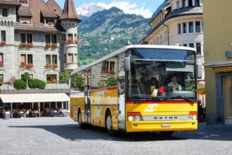 Bright yellow Swiss PostBus in a mountain town square, ideal for illustrating intercity and rural coach travel featured in the Busbud app guide.