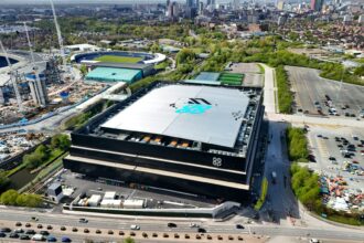 Aerial view of Co-op Live Manchester arena next to the Etihad Campus with the city skyline in the background.