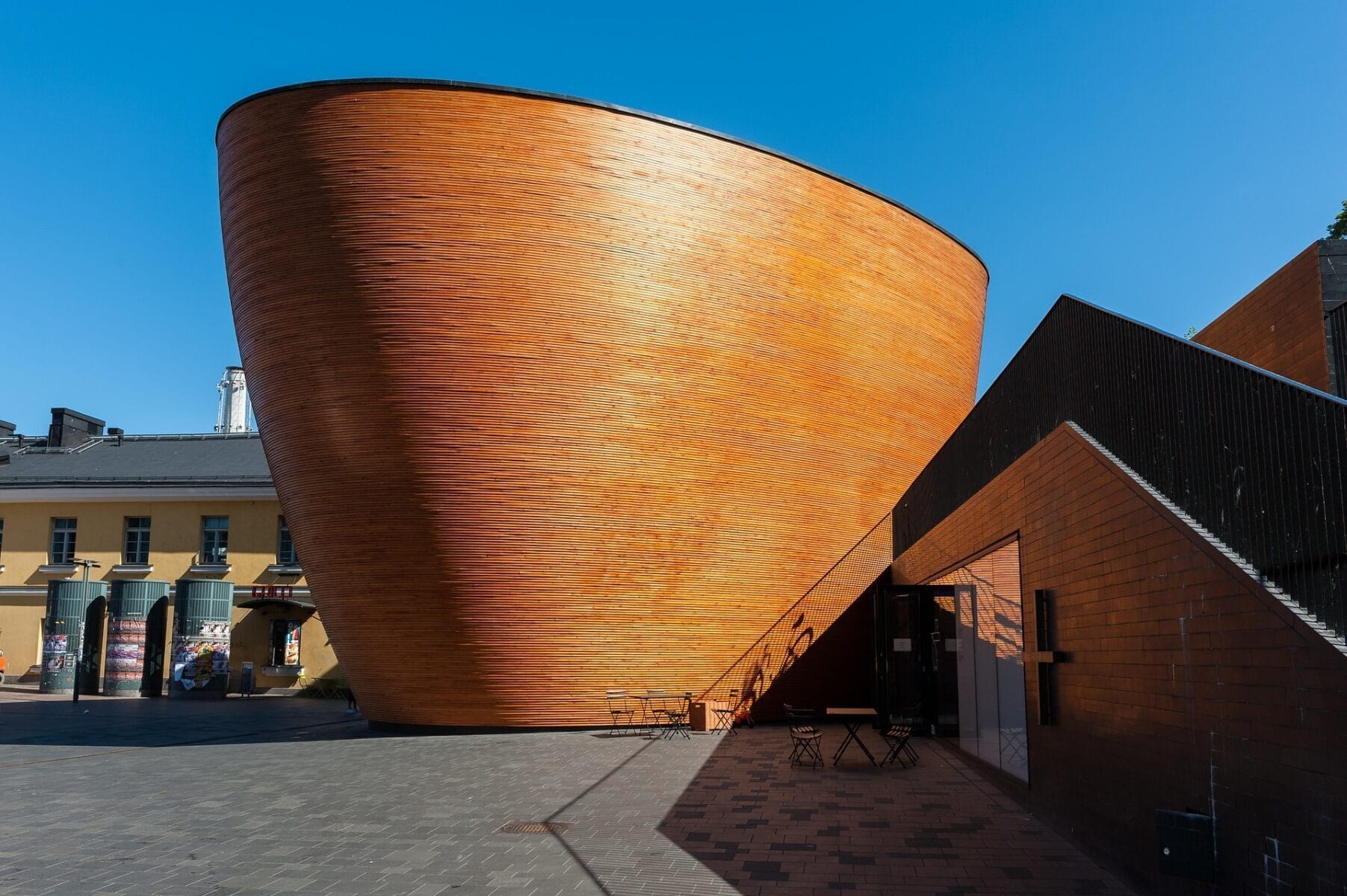 The Kamppi Chapel of Silence, a curved wooden structure glowing under bright sunlight in central Helsinki.