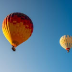 “Two colourful hot air balloons flying against a clear blue sky during a summer festival ascent.”