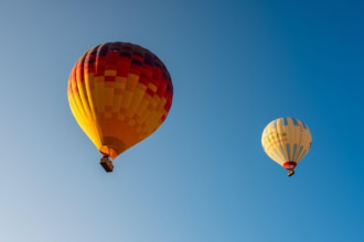 โTwo colourful hot air balloons flying against a clear blue sky during a summer festival ascent.โ