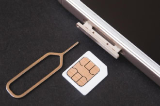 Close-up of a smartphone SIM card slot with a SIM ejector tool and SIM card on a black surface.