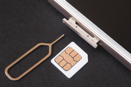 Close-up of a smartphone SIM card slot with a SIM ejector tool and SIM card on a black surface.