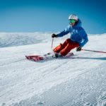 Skier carving on a groomed slope with clear blue skies.