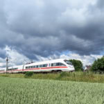 High-speed Deutsche Bahn ICE train travelling through green fields in Germany under a dramatic cloudy sky