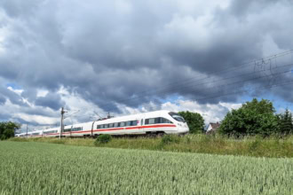 High-speed Deutsche Bahn ICE train travelling through green fields in Germany under a dramatic cloudy sky